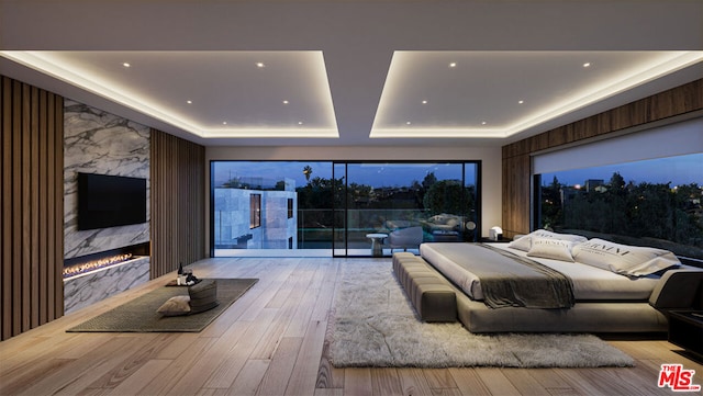 bedroom featuring a premium fireplace, a tray ceiling, and light hardwood / wood-style floors