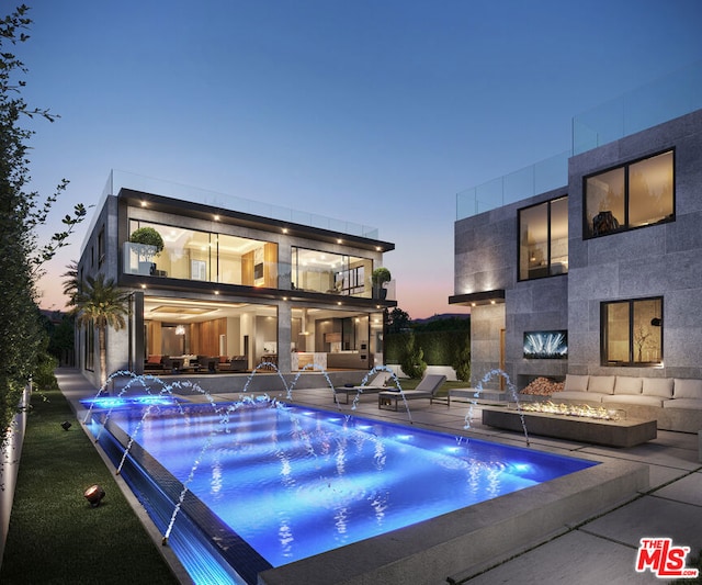 pool at dusk with pool water feature and a patio