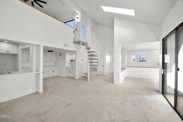 unfurnished living room featuring high vaulted ceiling, sink, light carpet, and a skylight