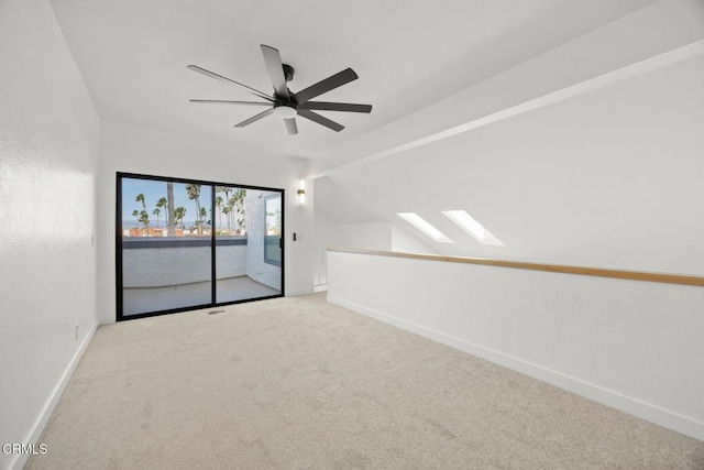 carpeted spare room featuring baseboards, lofted ceiling with skylight, and ceiling fan