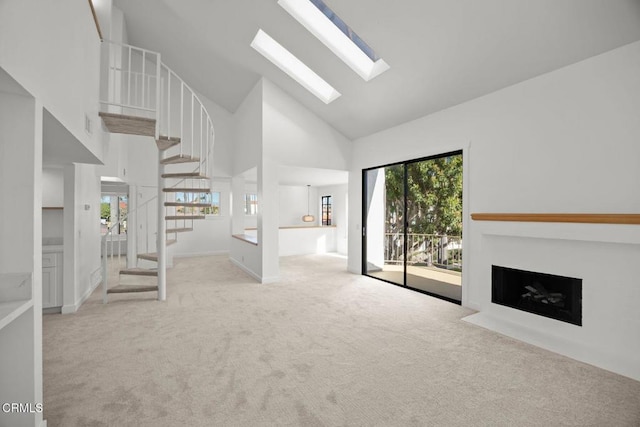 unfurnished living room featuring stairway, carpet floors, high vaulted ceiling, a skylight, and a fireplace with flush hearth