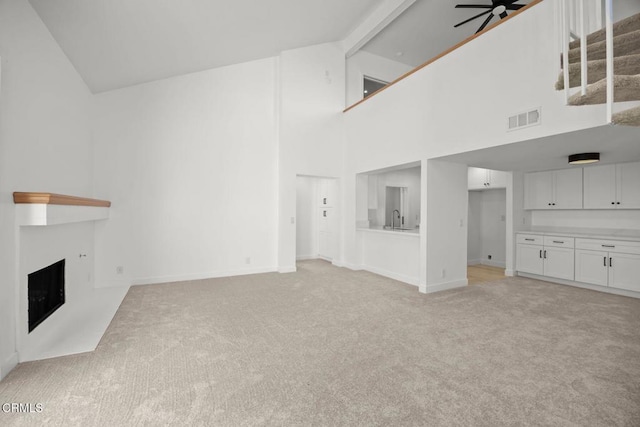 unfurnished living room featuring visible vents, ceiling fan, light carpet, a fireplace, and a sink