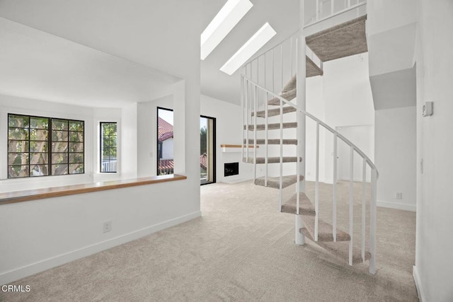 stairway featuring lofted ceiling with skylight, baseboards, and carpet