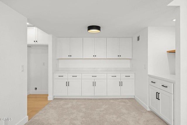 kitchen with visible vents, light carpet, white cabinets, light countertops, and baseboards