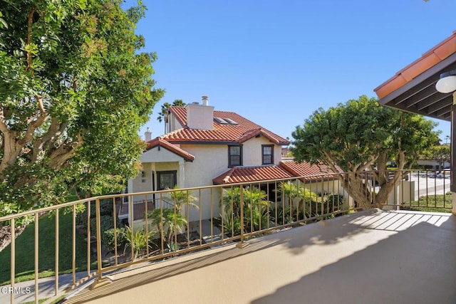 exterior space with a tiled roof, stucco siding, a balcony, and a chimney