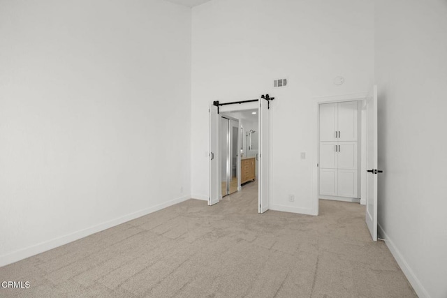 unfurnished bedroom with visible vents, light carpet, a barn door, baseboards, and a towering ceiling