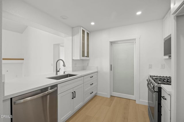 kitchen with light wood-style flooring, a sink, white cabinetry, appliances with stainless steel finishes, and glass insert cabinets