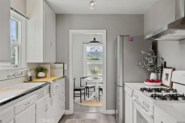 kitchen featuring white cabinets, wall chimney exhaust hood, sink, backsplash, and white gas range oven