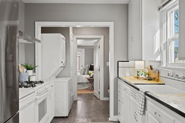 kitchen with gas range gas stove, backsplash, dark tile patterned flooring, stainless steel refrigerator, and white cabinets