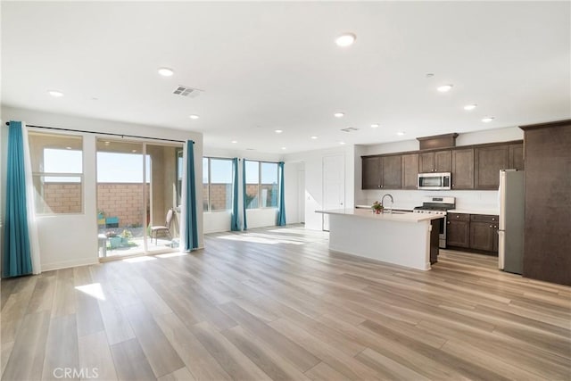 kitchen featuring a kitchen island with sink, light wood-type flooring, stainless steel appliances, and dark brown cabinetry