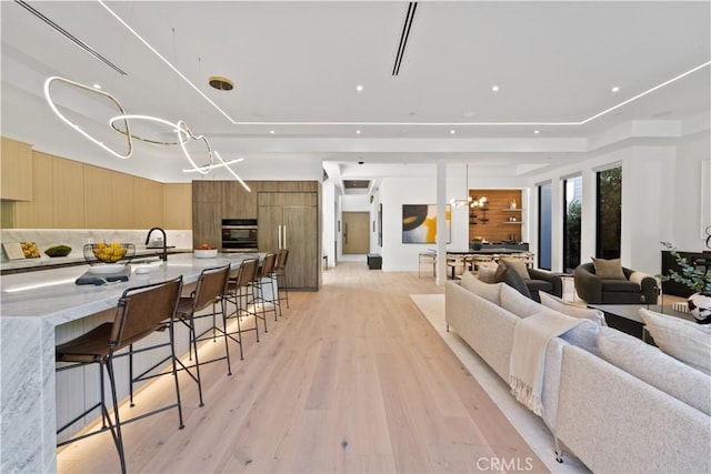 living room with light wood-type flooring, sink, a raised ceiling, and a notable chandelier