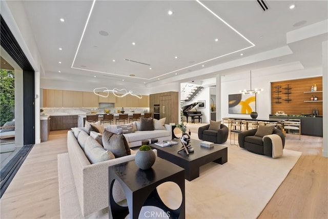 living room with light hardwood / wood-style floors, a raised ceiling, and a notable chandelier