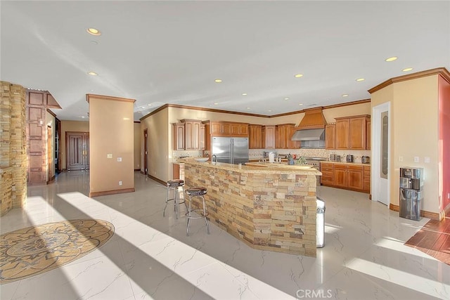 kitchen featuring built in fridge, custom exhaust hood, tasteful backsplash, a kitchen island with sink, and a breakfast bar