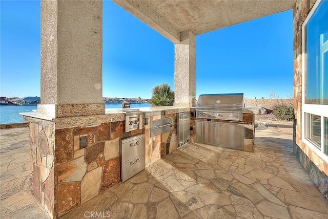 view of patio featuring exterior kitchen, a grill, and a water view