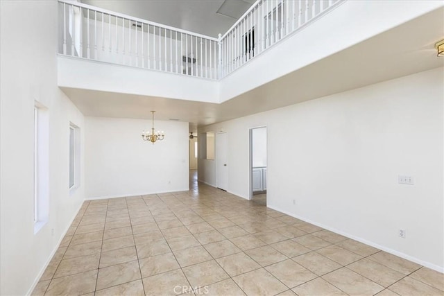 empty room featuring a notable chandelier, a towering ceiling, and light tile patterned flooring