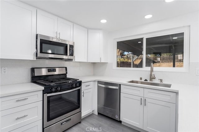 kitchen with light hardwood / wood-style floors, decorative backsplash, sink, white cabinetry, and appliances with stainless steel finishes