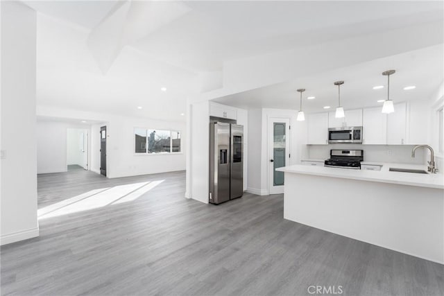 kitchen featuring white cabinetry, stainless steel appliances, hanging light fixtures, light hardwood / wood-style flooring, and sink