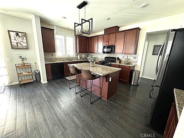 kitchen with dark wood-type flooring, hanging light fixtures, a kitchen island, black appliances, and a kitchen bar