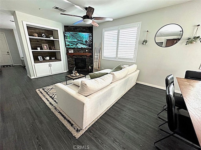 living room with a stone fireplace, dark hardwood / wood-style floors, ceiling fan, and built in shelves