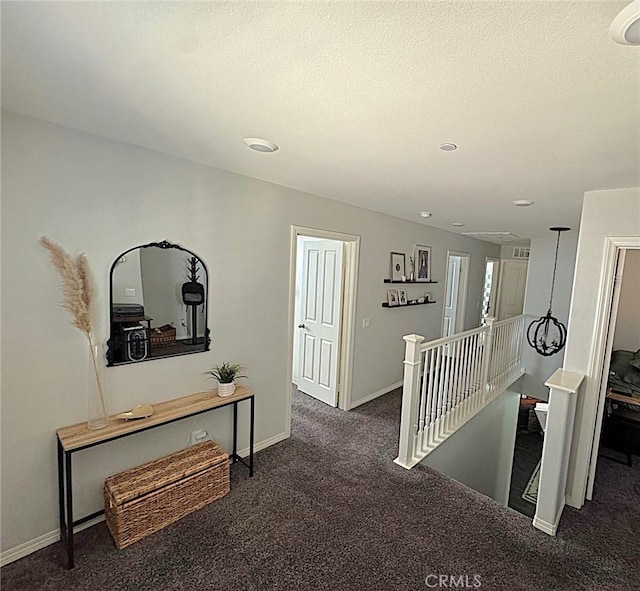 hallway with a textured ceiling and dark carpet