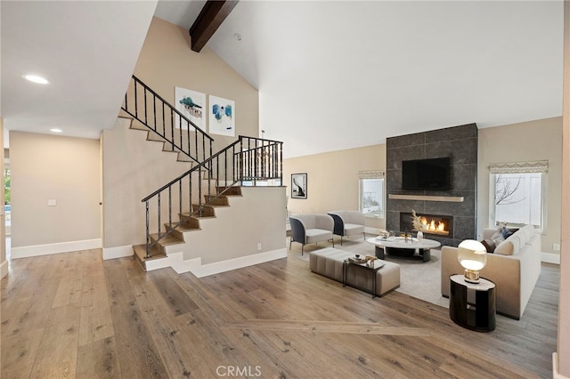 living room featuring vaulted ceiling with beams, hardwood / wood-style floors, and a tiled fireplace