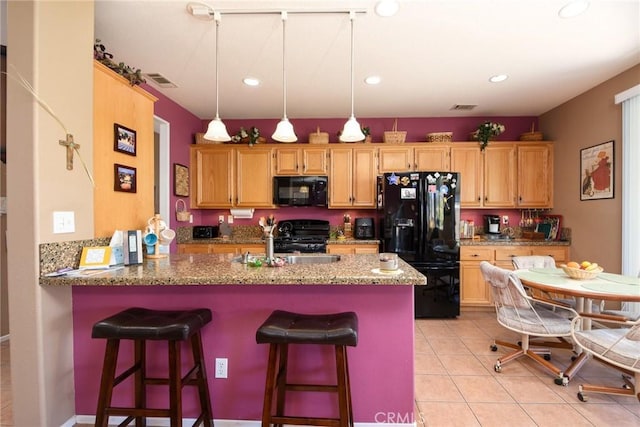 kitchen with black appliances, a breakfast bar, kitchen peninsula, light tile patterned floors, and light stone counters