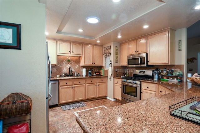 kitchen featuring appliances with stainless steel finishes, light brown cabinets, sink, backsplash, and light stone counters