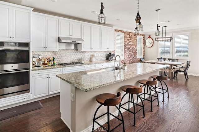 kitchen featuring pendant lighting, white cabinets, a kitchen breakfast bar, sink, and a center island with sink