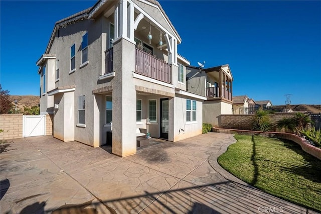 rear view of property with a yard, a balcony, and a patio