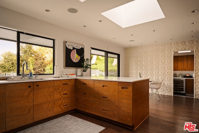 kitchen featuring wine cooler, dark hardwood / wood-style floors, kitchen peninsula, sink, and a skylight