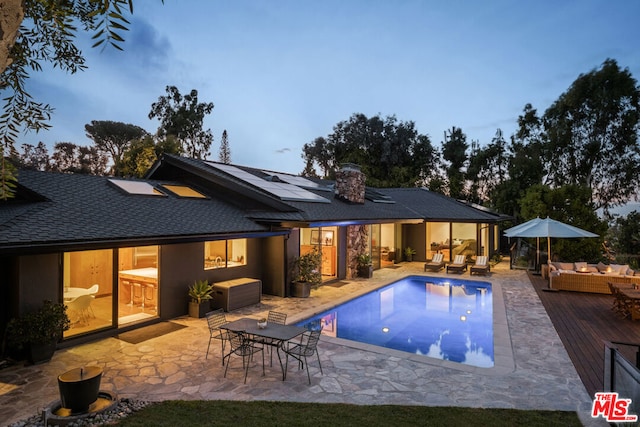 pool at dusk with an outdoor living space and a deck