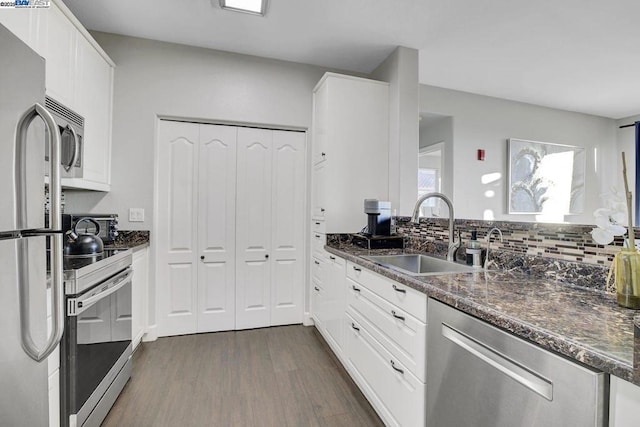 kitchen with appliances with stainless steel finishes, sink, white cabinetry, and dark stone counters