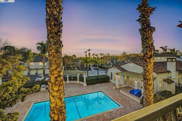 pool at dusk featuring a pergola and a patio