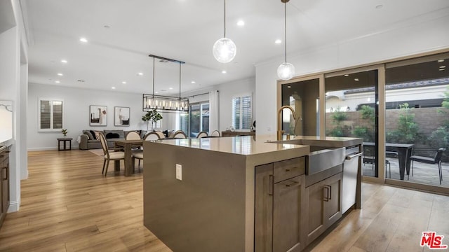 kitchen with light hardwood / wood-style floors, a kitchen island with sink, dishwasher, hanging light fixtures, and sink