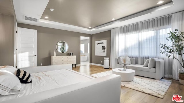 bedroom with multiple windows, a tray ceiling, and light hardwood / wood-style flooring