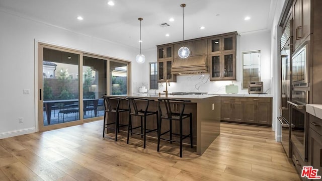 kitchen with light hardwood / wood-style flooring, tasteful backsplash, hanging light fixtures, a center island with sink, and crown molding