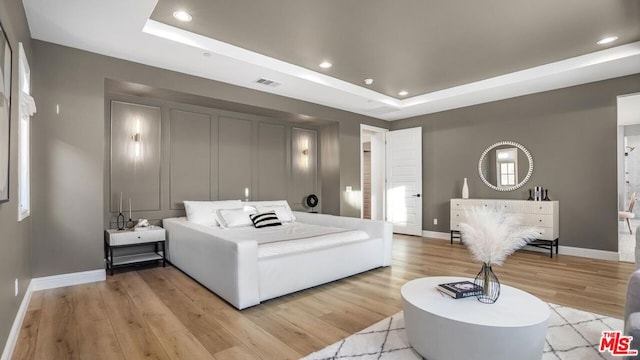 bedroom with light wood-type flooring and a tray ceiling