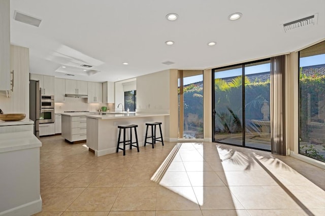 kitchen featuring floor to ceiling windows, a kitchen bar, a wealth of natural light, white cabinetry, and light tile patterned floors