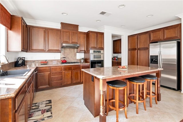 kitchen with stainless steel appliances, a center island, sink, and light stone counters