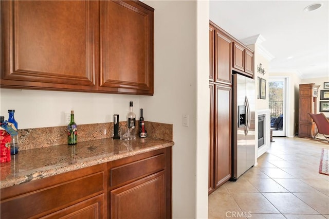 kitchen featuring light stone counters, stainless steel fridge, ornamental molding, and light tile patterned flooring