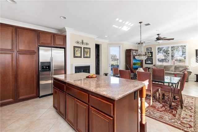 kitchen with light tile patterned floors, crown molding, stainless steel fridge, a center island, and light stone counters