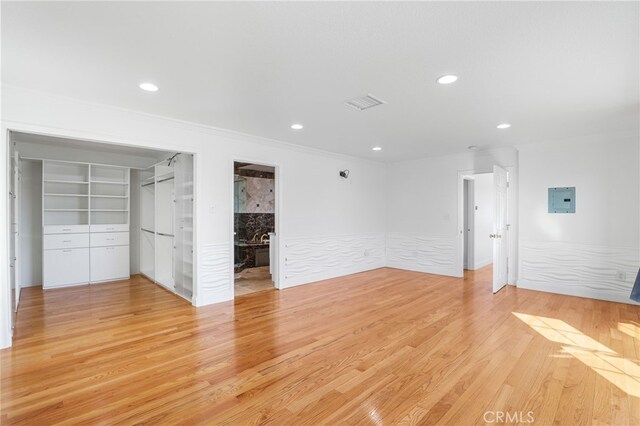 unfurnished bedroom with ensuite bathroom, light hardwood / wood-style floors, crown molding, a spacious closet, and a closet