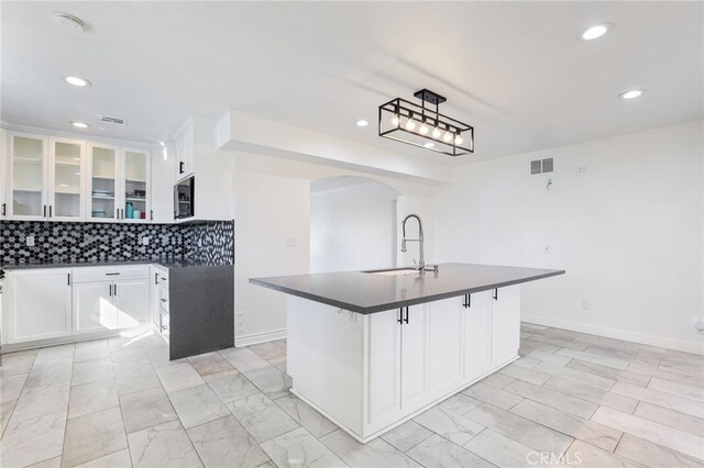 kitchen featuring decorative backsplash, sink, white cabinets, and a kitchen island with sink