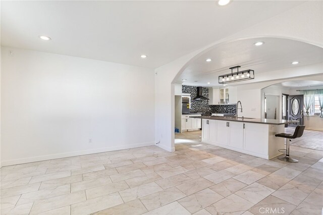 kitchen featuring wall chimney exhaust hood, sink, white cabinetry, and a center island with sink