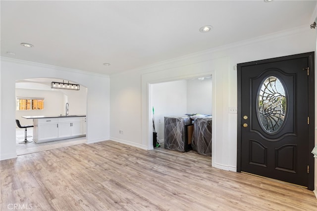 entrance foyer featuring arched walkways, light wood-type flooring, crown molding, and baseboards