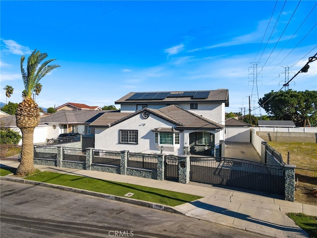 traditional-style home featuring stucco siding, a tile roof, a gate, a fenced front yard, and solar panels