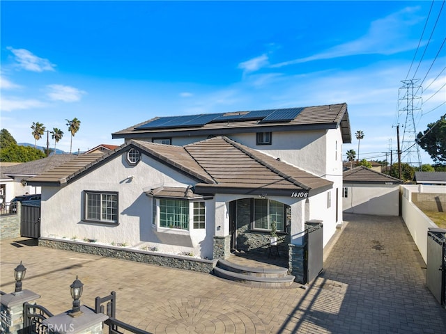 view of front of home featuring stucco siding, a patio, a fenced backyard, solar panels, and a tiled roof