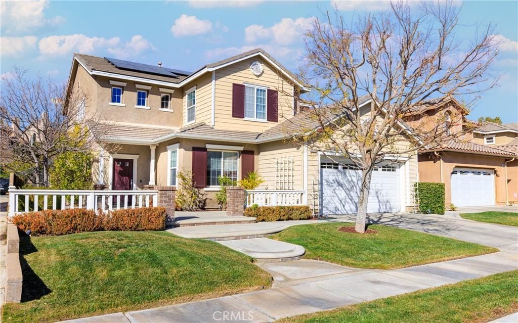 view of front of property featuring a front lawn, a garage, a porch, and solar panels