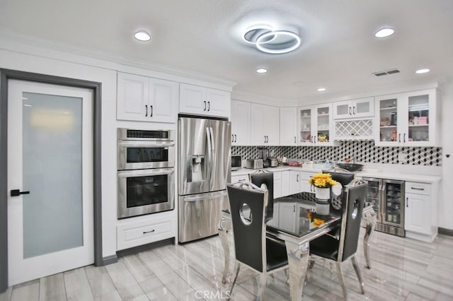 kitchen featuring appliances with stainless steel finishes, backsplash, wine cooler, ornamental molding, and white cabinets