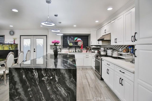 kitchen featuring pendant lighting, decorative backsplash, stainless steel gas range oven, white cabinets, and dark stone counters